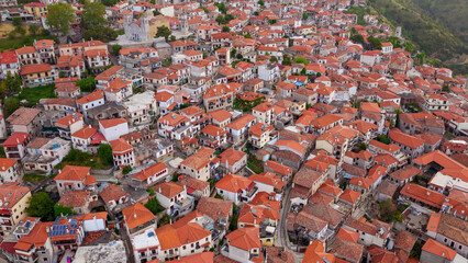 Naklejka premium Dimitsana village shows traditional architecture with many houses featuring distinct orange-red tiled roofs nestled into a lush green hillside, creating a dense pattern of classic greek habitation
