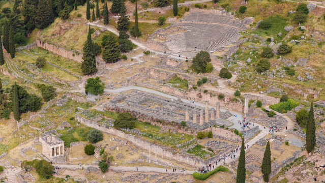 Delphi archaeological site presenting the reconstructed temple of Apollo ruins, the ancient theatre, and other historical structures attracting tourists visiting the sacred way in Greece