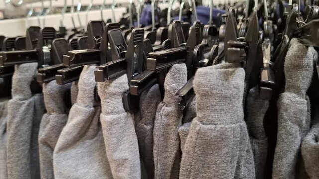 Row of grey sweatpants hanging on black plastic hangers with clips close up. Casual sporty clothing on garment rack in a retail store. Knitted trousers or joggers. Soft cotton apparel textiles