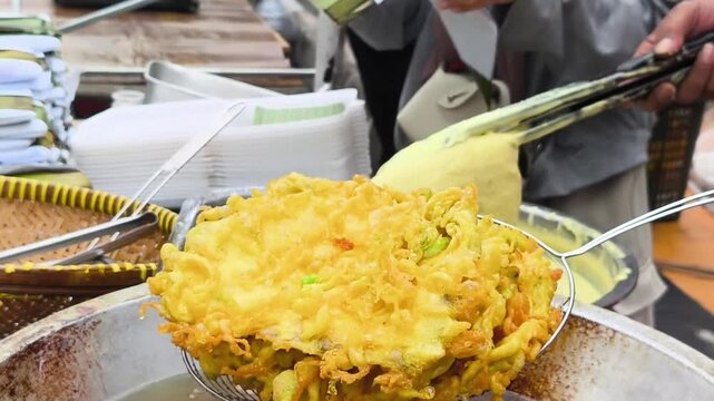 Close up of frying traditional Indonesian tempe mendoan in a large wok with hot sizzling cooking oil