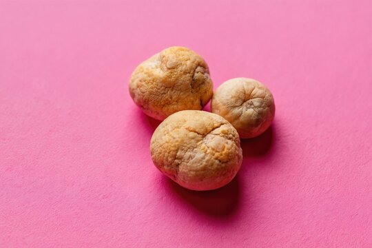 Three yellowish tonsil stones sit on pink textured background. These calcified masses can cause bad breath and discomfort. Medical reference or educational material.