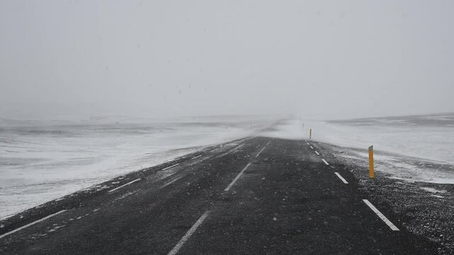 Point of view from a car driving on a lonely asphalt road during a heavy blizzard. Severe weather conditions and strong wind in iceland