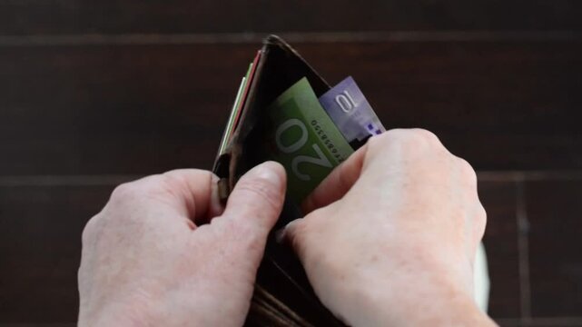 First person view of hands counting small amount of Canadian paper money from wallet. Personal finance concept showing budgeting, limited funds, spending, financial stress, or cost of living