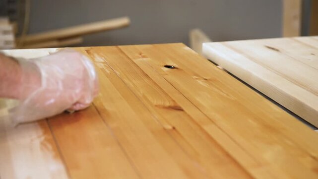 Master carpenter, Applying natural oil on natural wood product. Carpenter applying protective varnish to wooden surface in workshop. Impregnation of wood and coating with oil