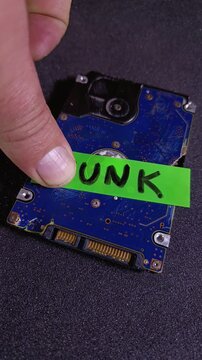 Vertical video of hand sticking a bright green junk note to a scrap hard drive. Concept of AI model collapse, corrupted data, e-waste recycling, system failure, broken and outdated equipment.