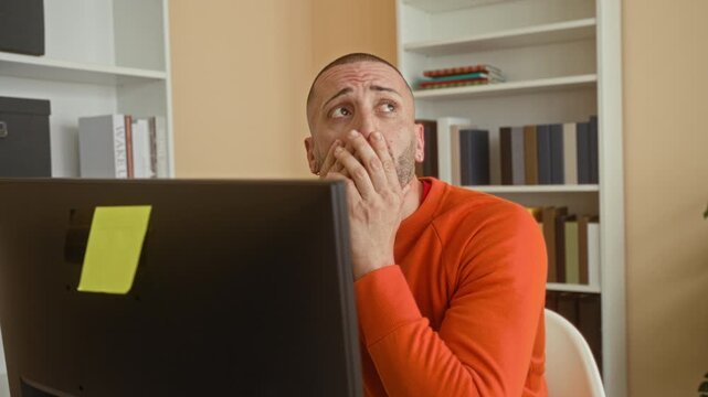 Man at computer frowning and squinting at the monitor, leaning forward with hands near keyboard in building; work frustration.