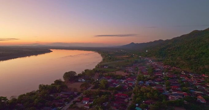 Drone perspective of Pak Kading at dusk, where warm orange and pink skies illuminate the river landscape and rural surroundings of Bolikhamxay Province.