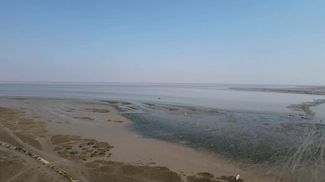 Aerial view of Nareri Lake with its vast muddy banks and calm waters under a clear blue sky in Sindh, Pakistan.