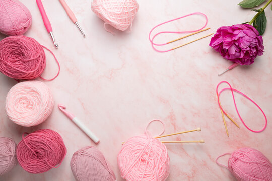 Pink themed, Grandmacore craft background.  Balls of yarn on a pink and white marbled surface with crochet hooks and knitting needles.  Slow crafting.