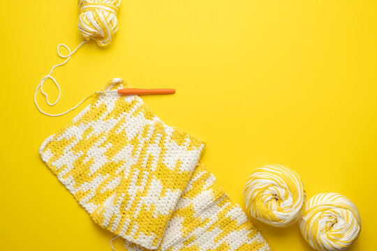 Yellow and white, crochet crafting with balls of yarn and hook on bright background.