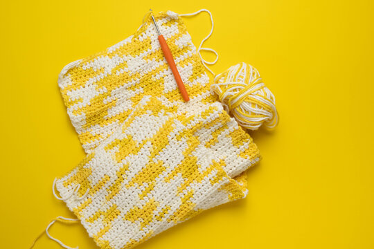 Yellow and white, crochet crafting with balls of yarn and hook on bright background.