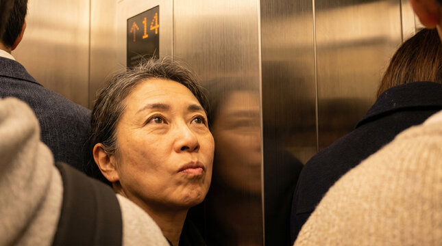 Annoyed mature Asian woman squished inside crowded elevator