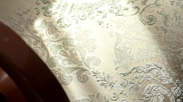 Elegant gold and silver damask fabric featuring an intricate floral pattern, with a soft beam of sunlight slowly moving across its detailed texture, creating a play of light and shadow
