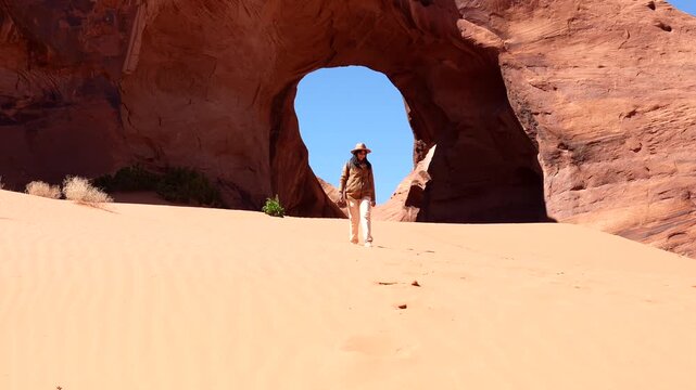 Young female traveler walking on a bright sunny day down a sand dune in monument valley near a natural sandstone arch on the utah arizona border, embodying adventure and exploration