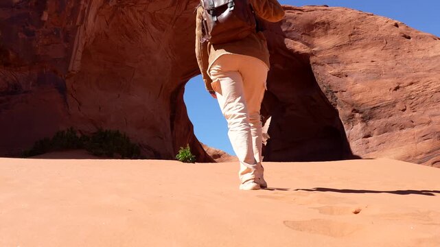 Young female traveler with a backpack and hat exploring the stunning ear of the wind arch, a natural sandstone formation in the iconic monument valley navajo tribal park, arizona utah border
