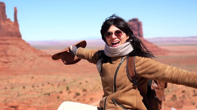 Young beautiful woman feeling freedom on a windy day, taking off her hat and enjoying the view of monument valley's majestic buttes from the famous forrest gump point on a sunny day