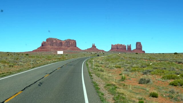 Iconic drive on highway 163 towards the stunning red sandstone buttes of monument valley tribal park, a famous cinematic landmark on the arizona utah border under a clear blue desert sky