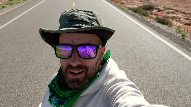 Happy tourist influencer vlogging with a selfie stick on the iconic road leading to monument valley, gesturing towards the famous buttes landscape during a sunny day road trip in arizona
