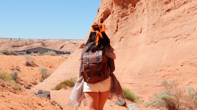 Smiling young woman with bandana and backpack navigating with a smartphone while hiking through red sandstone canyon near the famous arch cave in page, arizona, enjoying desert adventure