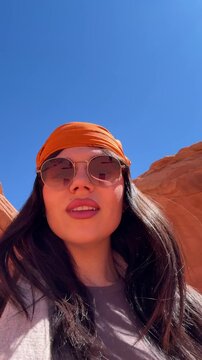Young beautiful woman vlogging and taking selfies in a stunning red rock slot canyon, enjoying her vacation and connecting with her followers under the bright desert sun in arizona