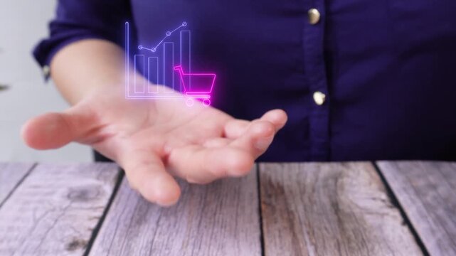 Market research and customer behavior. Close-up of a woman's hand at a table holding a virtual icon of a graphic with a shopping cart.