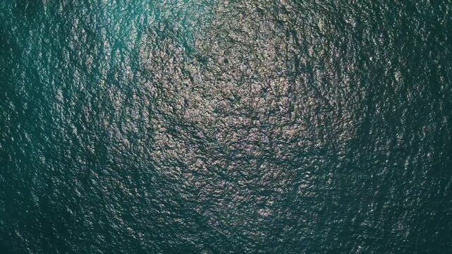 Top down aerial view of sparkling turquoise ocean water with sunlight reflections and rippling waves - 4K