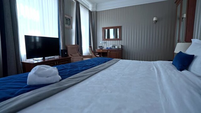 Elegant hotel room showcasing a comfortable king size bed with pristine white linens and blue accents, a television, and a classic wooden desk, creating a serene and inviting atmosphere