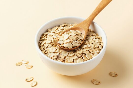 Bowl with oatmeal flakes and wooden spoon. Raw oat groats for healthy morning meal. Natural breakfast grain for energy. Cooking porridge ingredient.