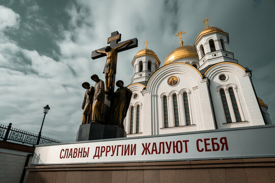 Crucifixion of Jesus Christ statue in front of a white Russian Orthodox Church with golden domes under a cloudy sky