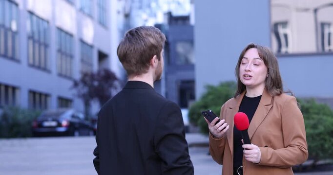 Professional journalist with microphone and smartphone interviewing man outdoors