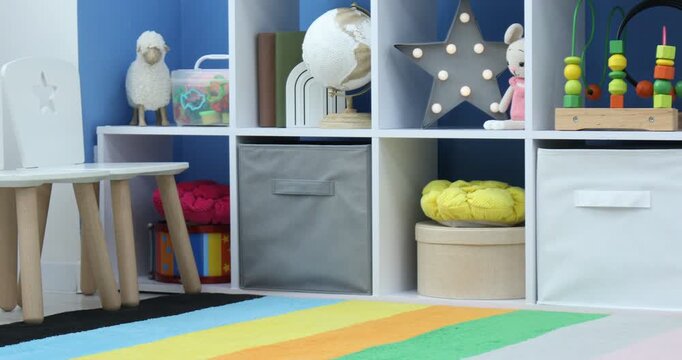 Shelving unit with different toys and decor near blue wall in child's room. Camera moving left