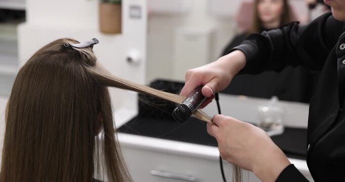 Stylist straightening woman's hair in beauty salon, closeup