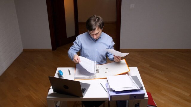 Man focusing on administrative work, sorting through numerous legal and financial papers, and maintaining detailed records within an orange binder on a light wooden desk