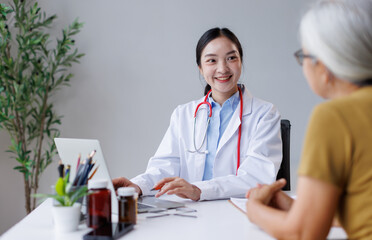 Obraz premium Young asian doctor providing medical consultation, smiling and discussing health information with an elderly patient during a routine check-up, offering professional support and care