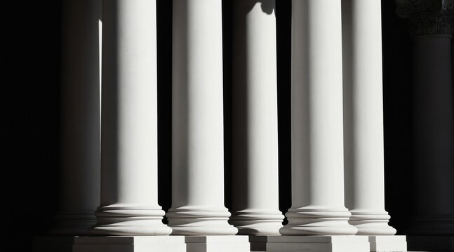 Row of white classical columns with strong shadows. Architectural elements on sunny day. Facade detail with stone pillars and ornate top parts.
