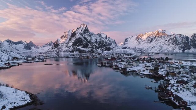 Aerial view of the snow-covered Lofoten mountains reflecting in the calm water of the fjord at sunset in Reine, Nordland, Norway.