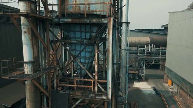 Cinematic aerial rising shot of a weathered industrial factory complex featuring heavy machinery and ventilation systems.