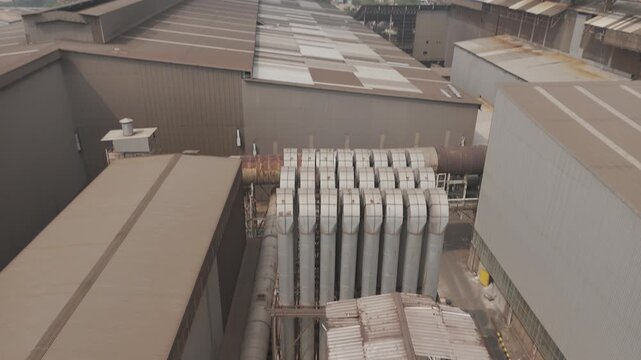 Shot in D-Log M for professional color grading Aerial drone shot rising above a large industrial factory plant with rusty metal silos and cooling pipes in jakarta