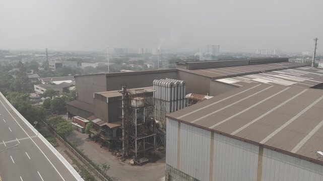 Shot in D-Log M for professional color grading Aerial view of large industrial factory plant next to empty highway in urban hazy landscape in jakarta