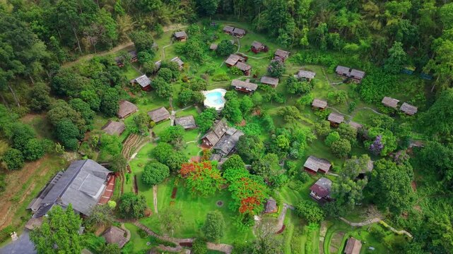 Cinematic aerial shot of a hidden tropical retreat featuring luxury wooden bungalows and a central pool integrated into a dense green forest Highlights peaceful sustainable travel in a regional distri