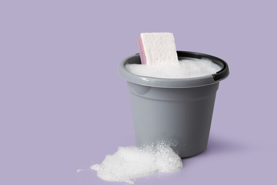 Plastic bucket of foam with sponge on purple background