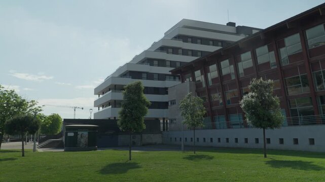 Low angle ground shot of contemporary mixed-use building with glass facade and brick exterior, green lawn in foreground, Gijon Spain.