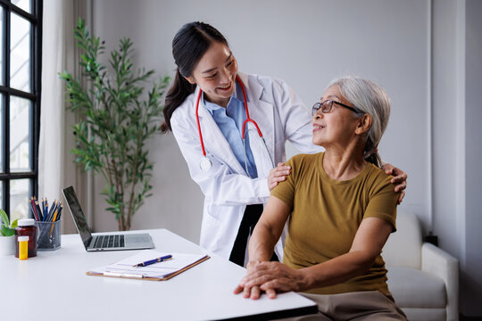 Asian female doctor providing comforting care closeness and support to a senior elderly patient during a medical checkup, discussing health and wellness in a clinic office setting