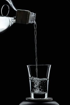 Liqueur is poured from a glass bottle into a shot glass, creating bubbles and splashes; high-speed motion photograph against a black background