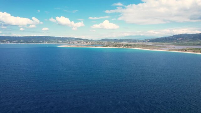 Aerial view of the turquoise coastline and sandy beach with mountains under a blue sky Paralia Ofriniou, Greece.