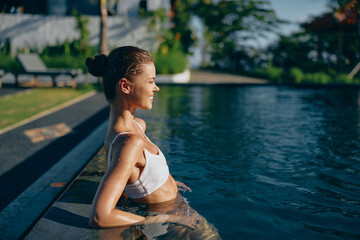 Obraz premium A woman relaxes at the pool edge, shoulders above water, enjoying warm sunlight. A lifestyle moment that conveys leisure, calm, and wellness in a bright outdoor setting.