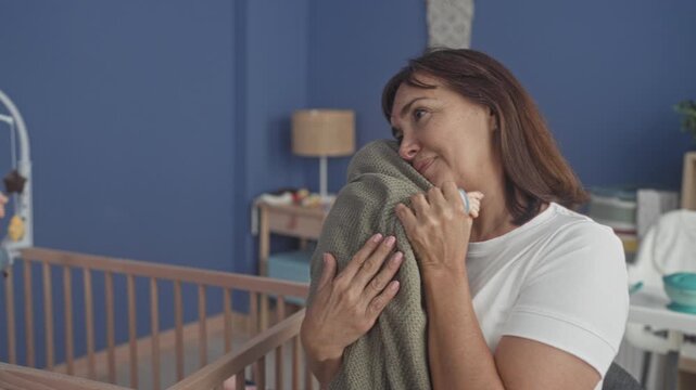 Woman cradling baby wrapped in blanket, hands holding swaddle against chest in building nursery; maternal comfort serenity.