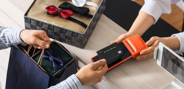 Female seller receiving payment for bow ties from man in boutique, top view