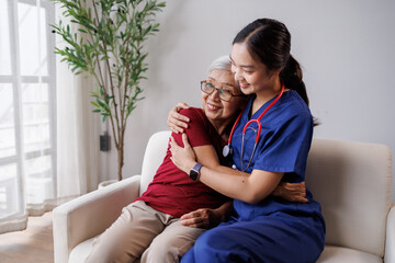 Young female caregiver or nurse in blue scrubs gently hugging and comforting a happy senior asian woman, showing support, empathy, and professional healthcare assistance at home © David