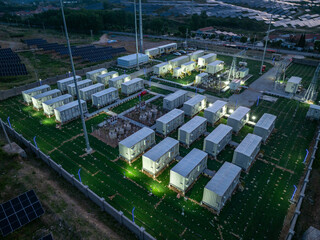 Fototapeta premium Aerial view of a large-scale energy storage power station operating at night with illuminated container modules and surrounding solar panels